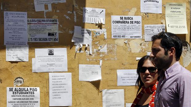 Una pareja pasa frente a una pared llena de anuncios de alquiler
