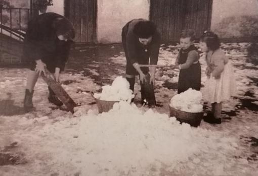 Dos mujeres recogen la nieve de una azotea mientras dos pequeños se divierten a su lado